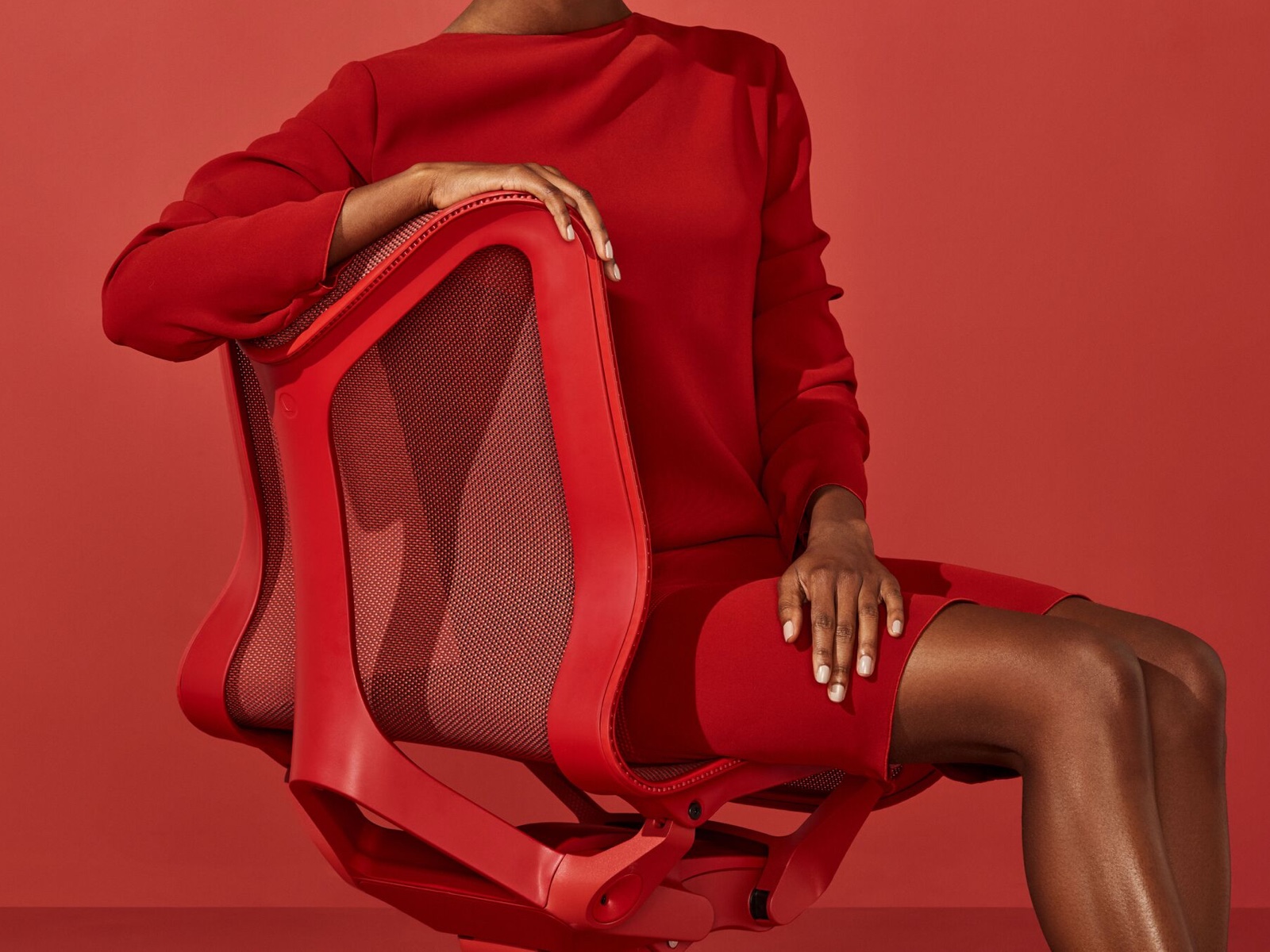 Una donna con un vestito rosso siede su una sedia Cosm con il fondo basso rosso Canyon.
